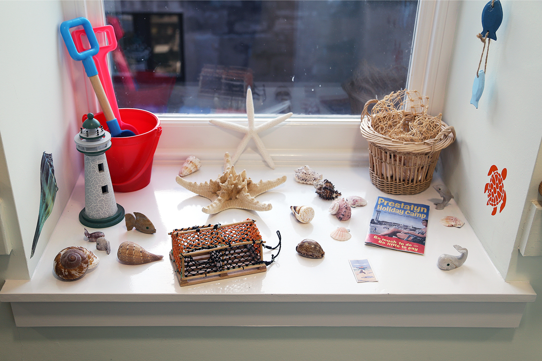 A windowsill set up as a beach scene, with shells and model lighthouse